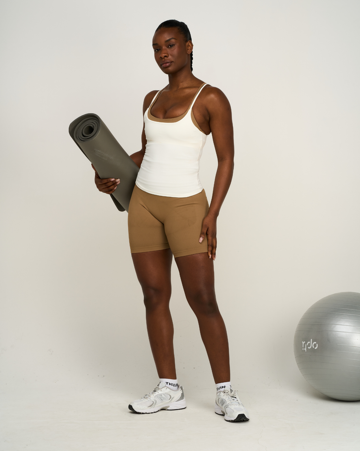 Elevate Sculpting Seamless Scoop Neck Cami in Cream, front view holding yoga mat, styled with brown shorts