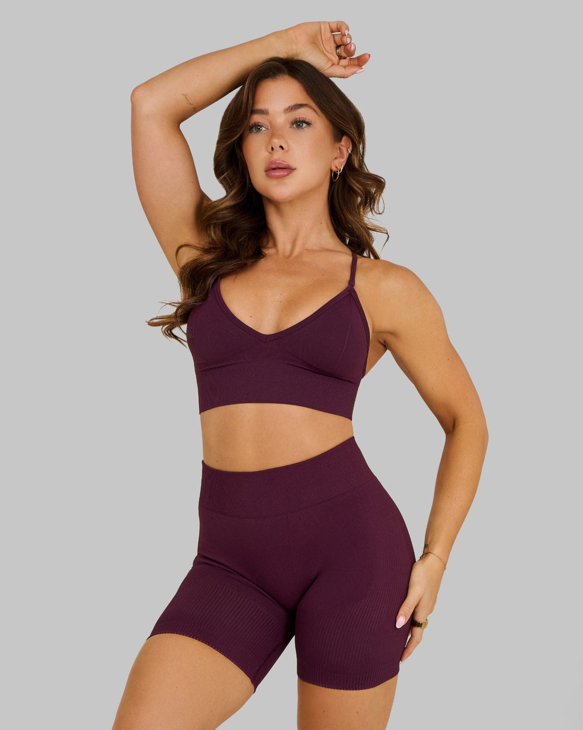 Elevate Multiway Sculpt Seamless Bra in Winter Plum Red, front view with arm raised, styled with shorts