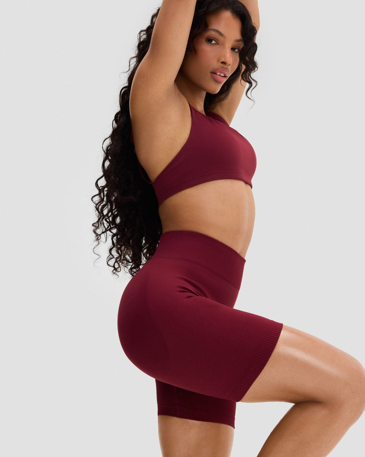 Elevate Sculpting Mid Waist Scrunch Shorts in Fine Wine Red, three-quarter front view with raised knee and mid waist